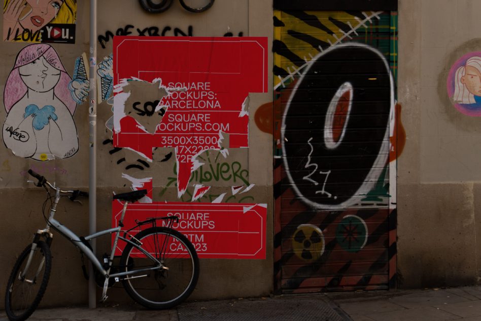 Red square poster with torn edges on wall by bicycle street art scene